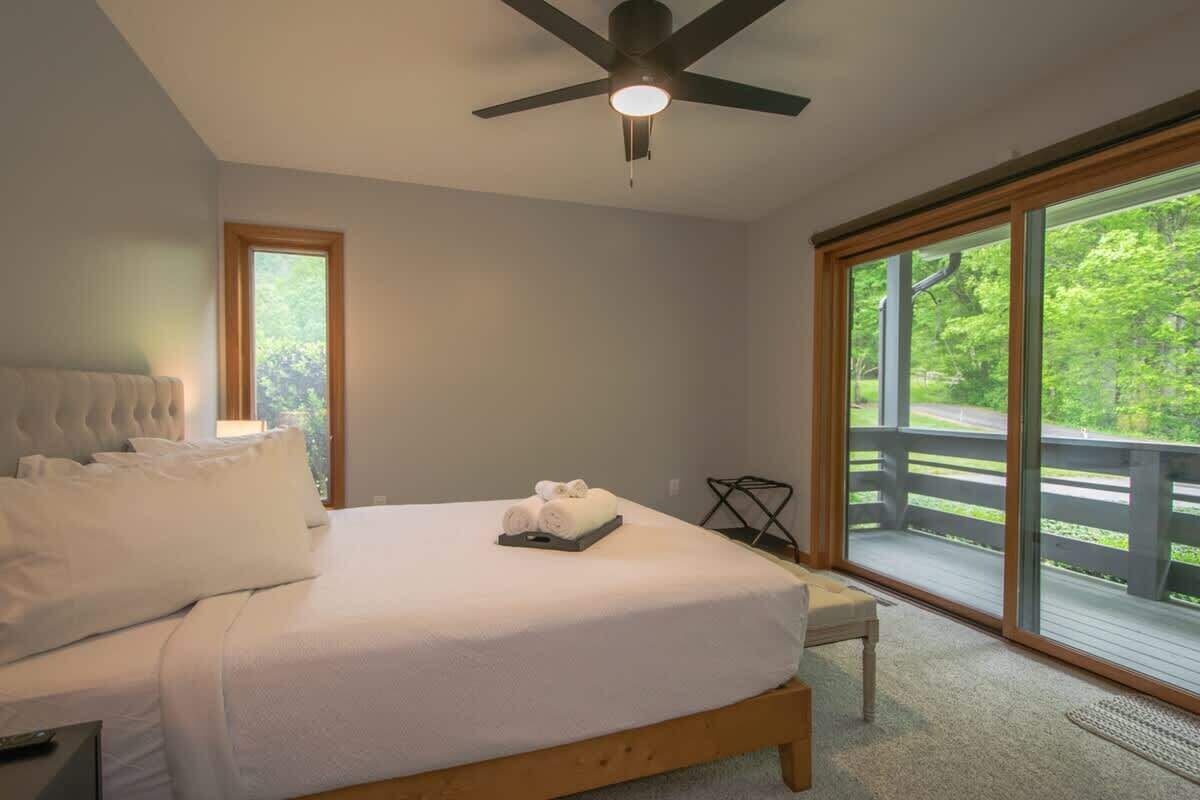 Ein Schlafzimmer mit Bett, Deckenventilator, Fenster und Blick auf eine Terrasse.