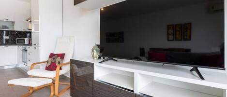 Uma sala de estar moderna com uma televisão de tela plana grande, um sofá branco e uma cadeira de madeira.
