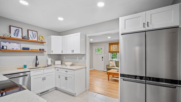 A modern kitchen with white cabinets, stainless steel appliances, and wooden shelves.