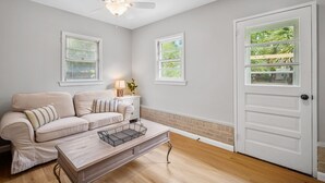 A living room with a beige sofa, a wooden coffee table, a ceiling fan, and a white door with a window.