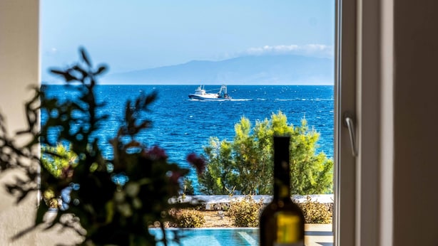 A view from inside a room with a window overlooking a body of water, a boat, and a mountain in the distance. - Golden View Villa in Golden Beach With Private Swimming Pool (Paros)