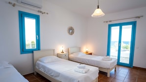 A room with two single beds, a large window with blue trim, a ceiling fan, and a view of the sea. - Golden View Villa in Golden Beach With Private Swimming Pool (Paros)