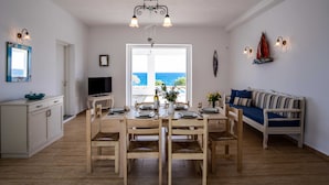 A dining area with a wooden table and chairs, a television, and a view of the sea through a large window. - Golden View Villa in Golden Beach With Private Swimming Pool (Paros)