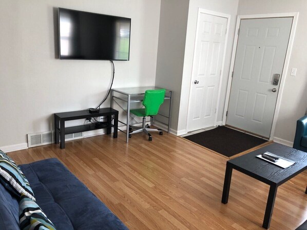 Sala de estar com televisão na parede, escrivaninha com cadeira, sofá e mesa de centro.