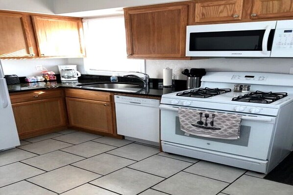 A compact kitchen with wooden cabinets, a white microwave, a gas stove, and a dishwasher.