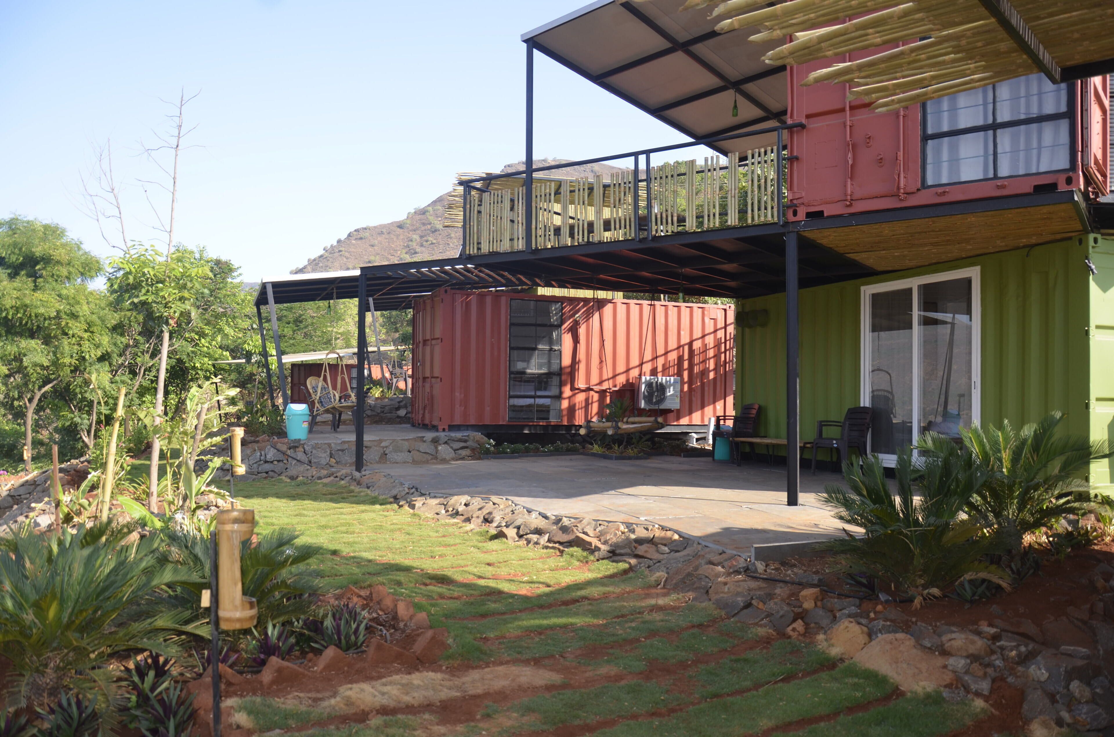 Ein Haus mit überdachter Terrasse, einer kleinen Sitzgelegenheit im Freien und einem Garten mit verschiedenen Pflanzen.