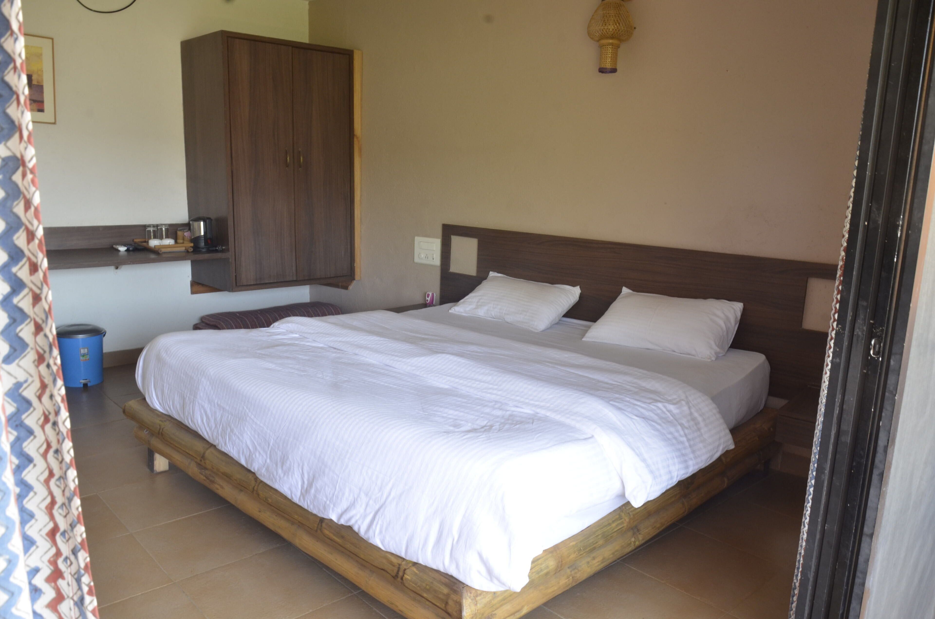 A bedroom with a wooden bed, white bedding, a wardrobe, and a small shelf with items.