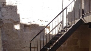 A staircase with a metal railing leading to an upper level. The walls are made of rough stone, and the floor is tiled with terracotta tiles.