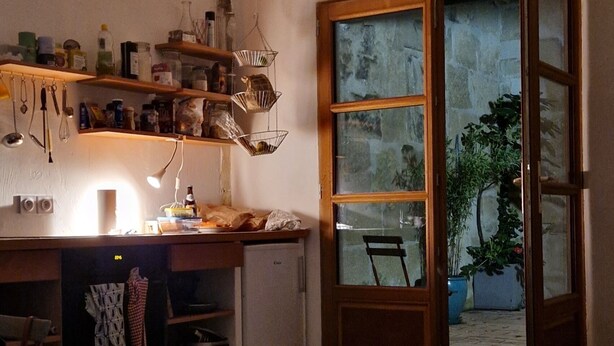 A compact kitchen with a built-in refrigerator, wooden shelves, and a dining area with a chair.