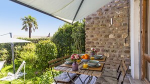 An outdoor dining area with a stone wall, a table set with plates, bowls, and a vase of flowers. - Maison Lamina - Welkeys (Anglet)