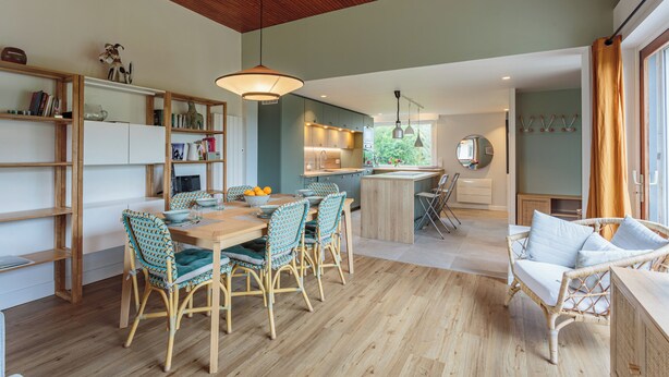 A modern kitchen with wooden cabinets, a dining area with wicker chairs, and a cozy seating area with a wicker sofa. - Maison Lamina - Welkeys (Anglet)