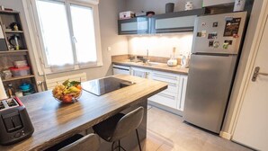 A modern kitchen with a wooden countertop, two bar stools, a built-in oven, a stainless steel refrigerator, and a window providing natural light.