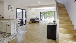 A spacious living area with a wooden staircase, a kitchen with bar stools, and a sliding glass door leading to an outdoor patio. - Villa Miarritze - Welkeys (Biarritz)