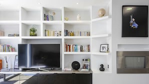 A modern living room with a large flat-screen TV, a bookshelf filled with books, a decorative globe, and a framed picture on the wall. - Villa Miarritze - Welkeys (Biarritz)