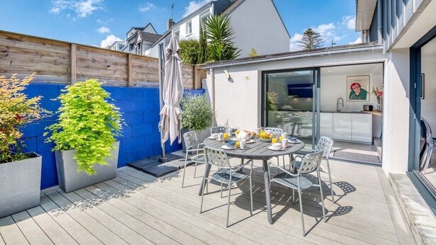 Eine moderne Terrasse mit Esstisch für zwei Personen, umgeben von Topfpflanzen und einer Holzterrasse.