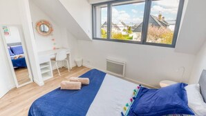 Ein Schlafzimmer mit Bett, Schreibtisch, Stuhl und einem Fenster mit Blick auf Häuser.