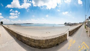 Ein Strand mit einer Steinmauer, einem gepflasterten Weg und blauem Himmel.