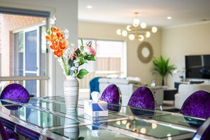A dining area with a glass table, purple chairs, a vase with flowers, and a chandelier. - Broadstone PC 9-bed 5-bathroom Luxe Family House Double Storey (Point Cook)