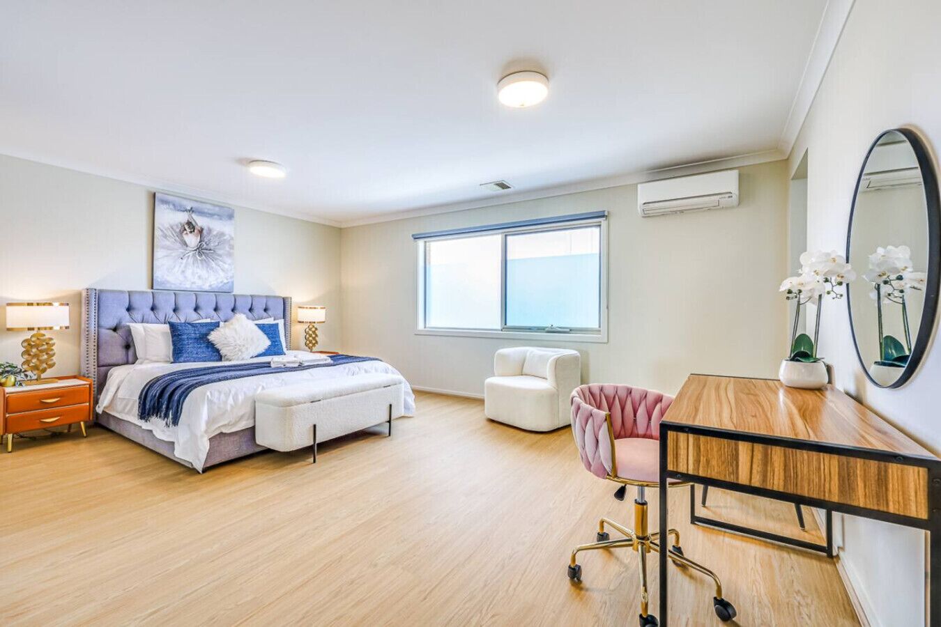 A bedroom with a bed, bedside tables, a desk, a chair, a window, and an air conditioning unit.