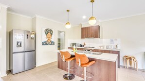 Cocina moderna con refrigerador, pileta doble y dos taburetes de bar.