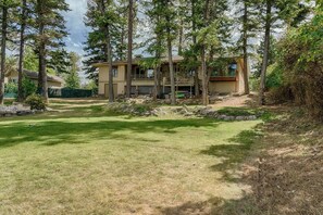 A two-story house with a covered patio area, surrounded by a well-maintained lawn and tall trees. - Love on Lilac Lake, Private Dock and Lake Access (Kalispell)