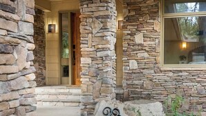 A stone exterior with a number '23' sign, a wooden door, and a window with a view of trees. - Love on Lilac Lake, Private Dock and Lake Access (Kalispell)