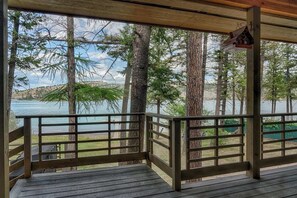 A wooden deck with a railing overlooking a lake, surrounded by tall trees.