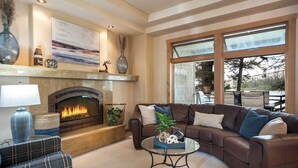A living room with a fireplace, a large window, and a view of the outdoors. - Love on Lilac Lake, Private Dock and Lake Access (Kalispell)