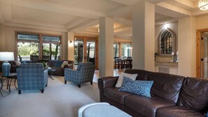 A spacious living room with a brown leather sofa, blue plaid armchairs, and a dining area visible through glass doors. - Love on Lilac Lake, Private Dock and Lake Access (Kalispell)