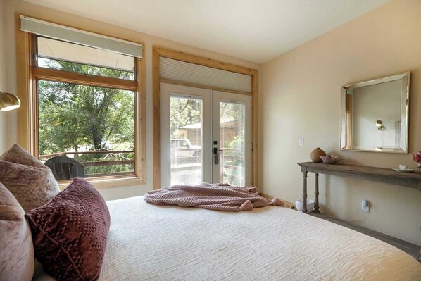 A bedroom with a large bed, a dresser, a mirror, and a window with a view of trees.
