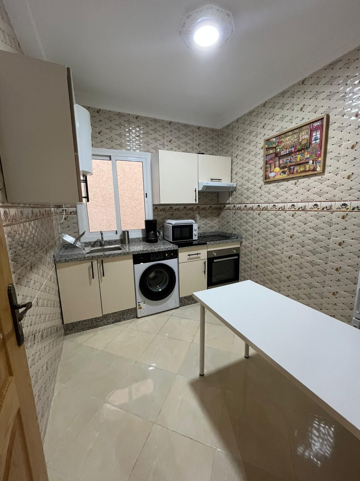 A compact kitchen with a washing machine, microwave, oven, and a dining table.