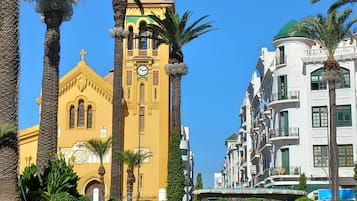 A yellow church with a clock tower, surrounded by palm trees and a flower garden.
