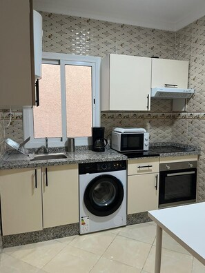 A compact kitchen with a washing machine, microwave, and a coffee maker.