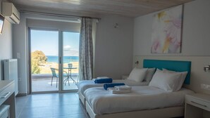 A bedroom with a bed, a nightstand, a TV, a desk, and a view of the beach. - Enali Villas-Villa Artemi (Κίσσαμος)