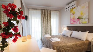 A hotel room with a bed, a bedside table, a vase with red flowers, a wall-mounted air conditioner, and a painting of flowers. - Enali Villas-Villa Artemi (Κίσσαμος)