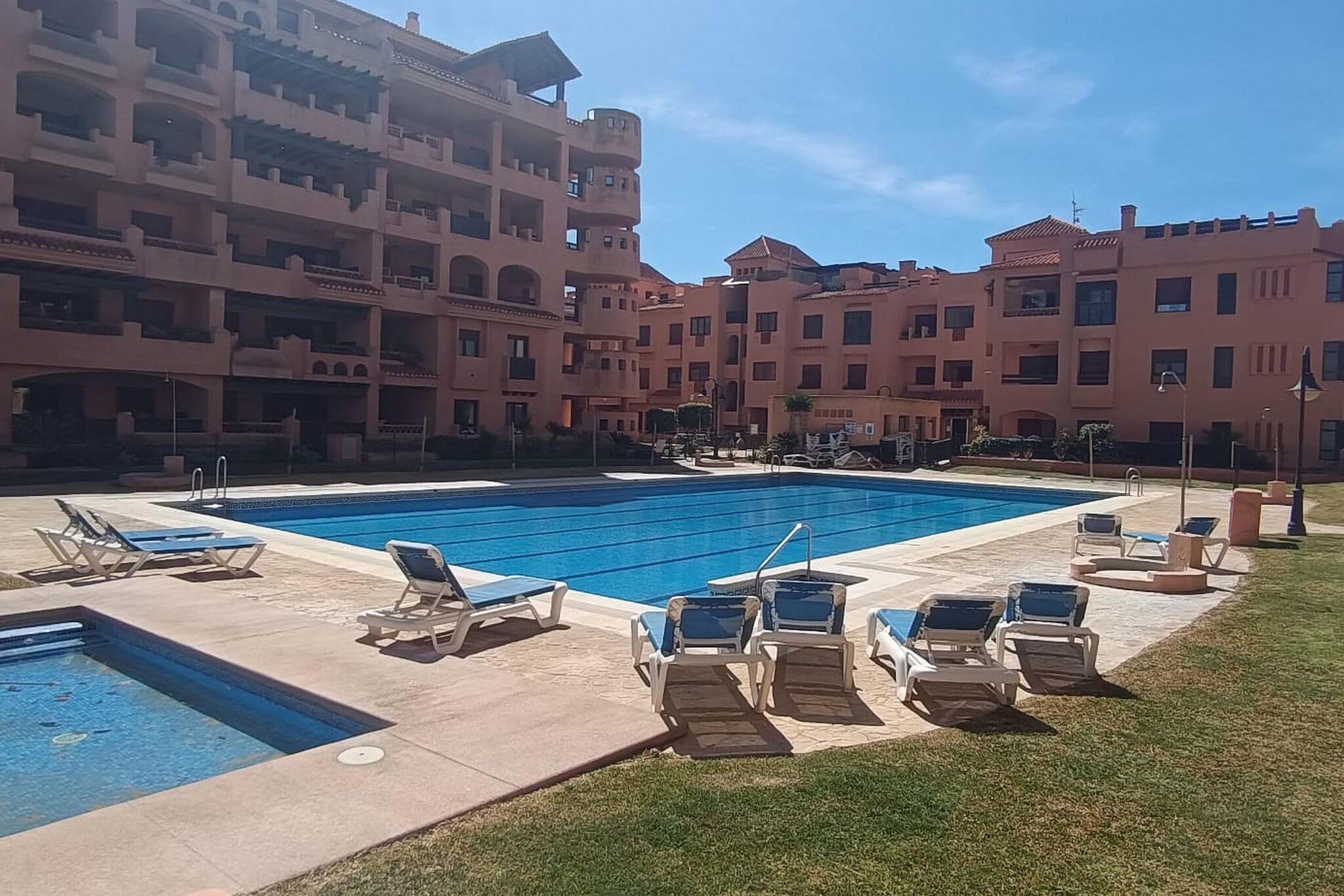 A swimming pool with lounge chairs and a building with multiple balconies in the background.