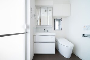 A compact bathroom with a white sink, mirror, and toilet. - TORA HOTEL Sensoji SUNNY (Tokyo)
