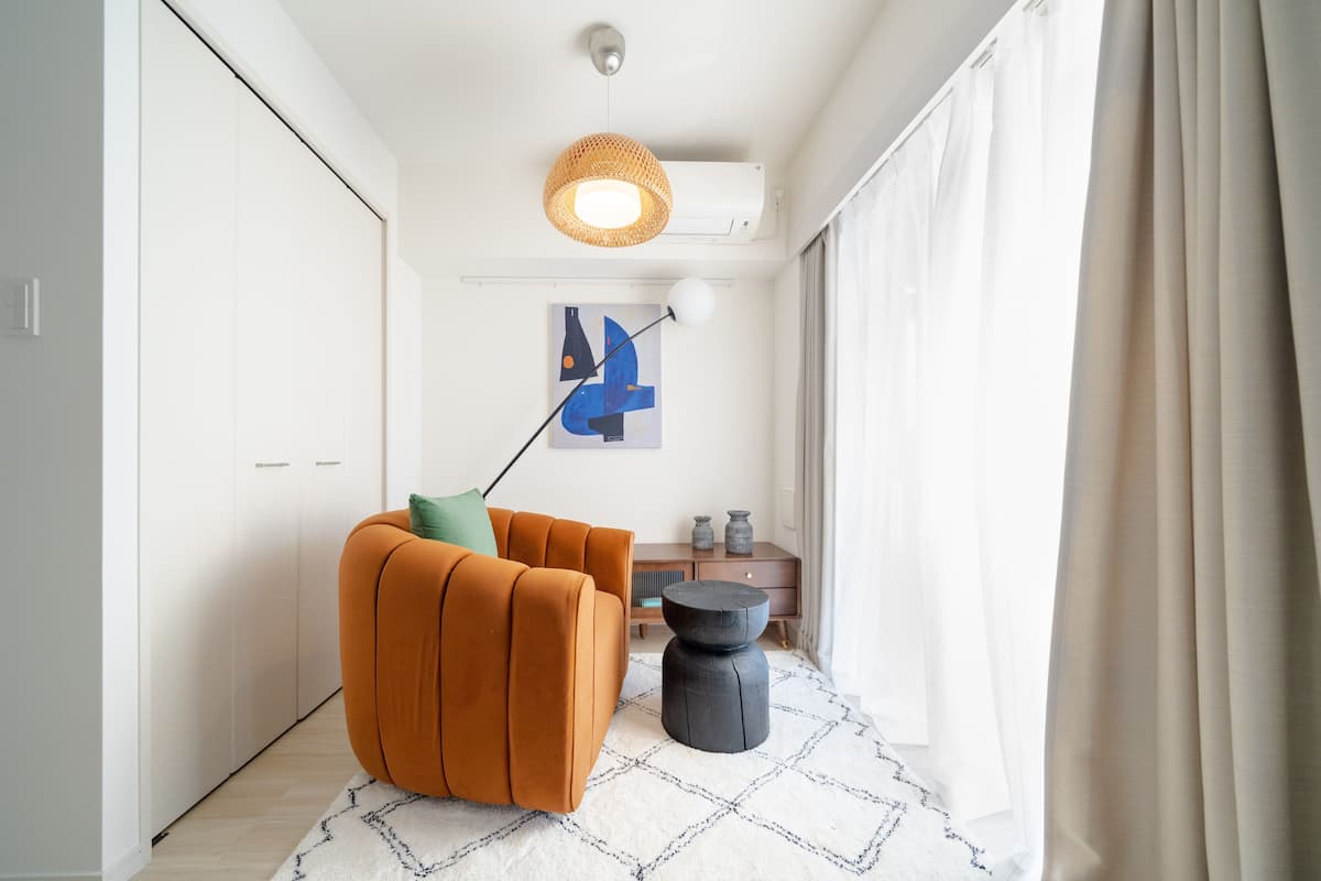 A modern living room with a sofa, a round black ottoman, a hanging light fixture, and a painting on the wall.