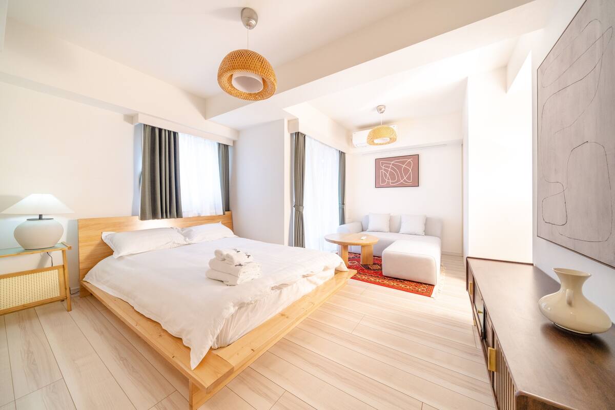 A modern hotel room with a wooden bed, a small round table, a sofa, and a large abstract painting on the wall.