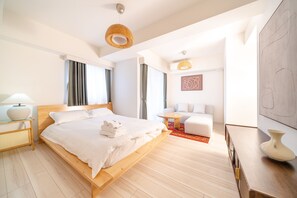 Moderni hotellihuone, jossa on puinen sänky, pieni pyöreä pöytä, sohva ja suuri abstrakti maalaus seinällä.
