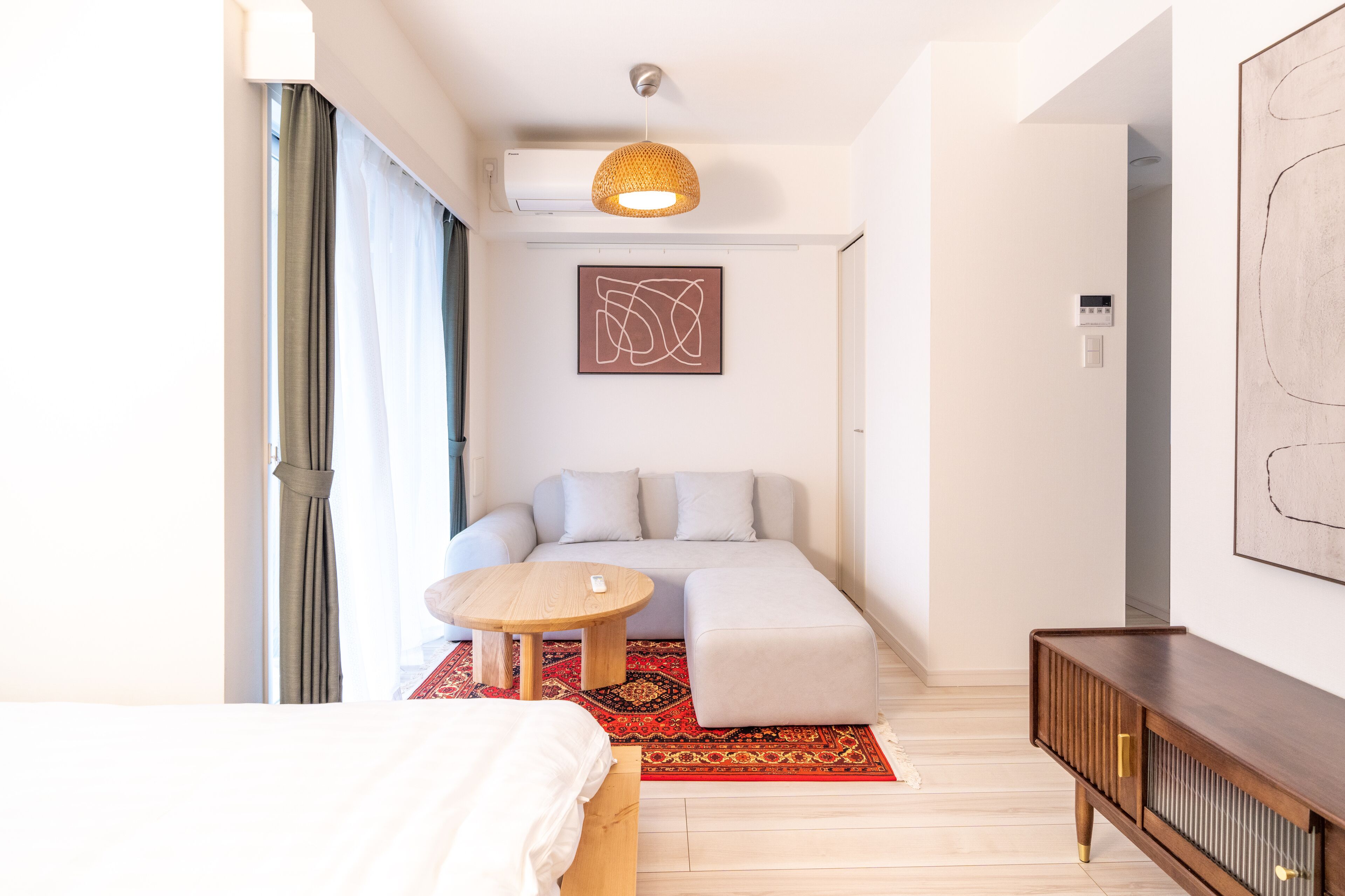 A modern hotel room with a bed, a sofa, a small table, a wooden sideboard, and a large abstract painting on the wall.
