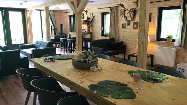 A wooden interior with a long dining table, black chairs, and a cozy seating area with sofas and a coffee table. - Ferienhaus im Sauerland (Winterberg)