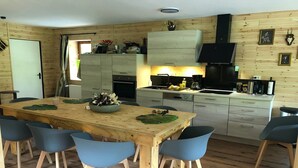 A wooden-paneled kitchen with a central island, a dining area with blue chairs, and a built-in oven. - Ferienhaus im Sauerland (Winterberg)
