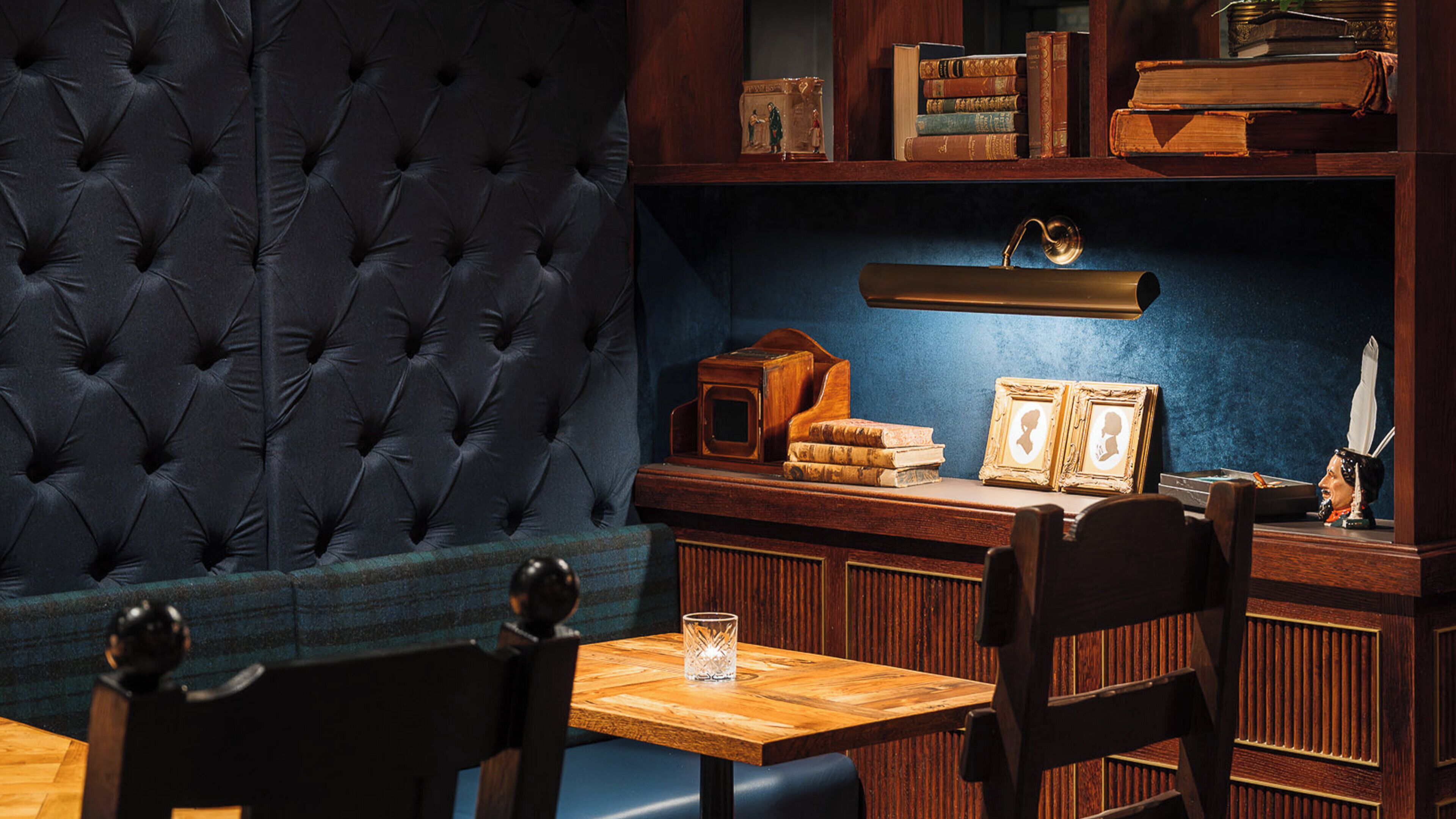Ein Zimmer mit einer gepolsterten Kopfteile, einem Holztisch mit Büchern und einer Lampe sowie einem Glas auf dem Tisch.