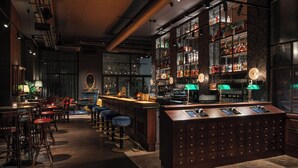 A bar area with stools, a counter, and shelves stocked with bottles. - Ruby Stella Hotel London by IHG (London)
