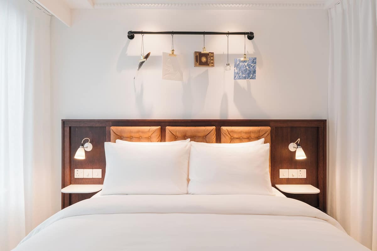 A neatly made bed with a wooden headboard, bedside lamps, and a wall-mounted light fixture.