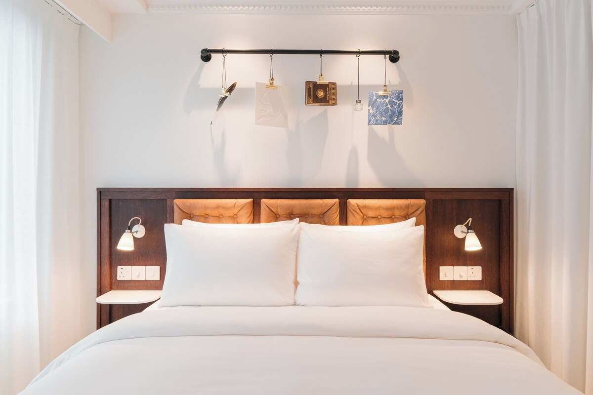 A neatly made bed with a wooden headboard, bedside lamps, and a wall-mounted light fixture.