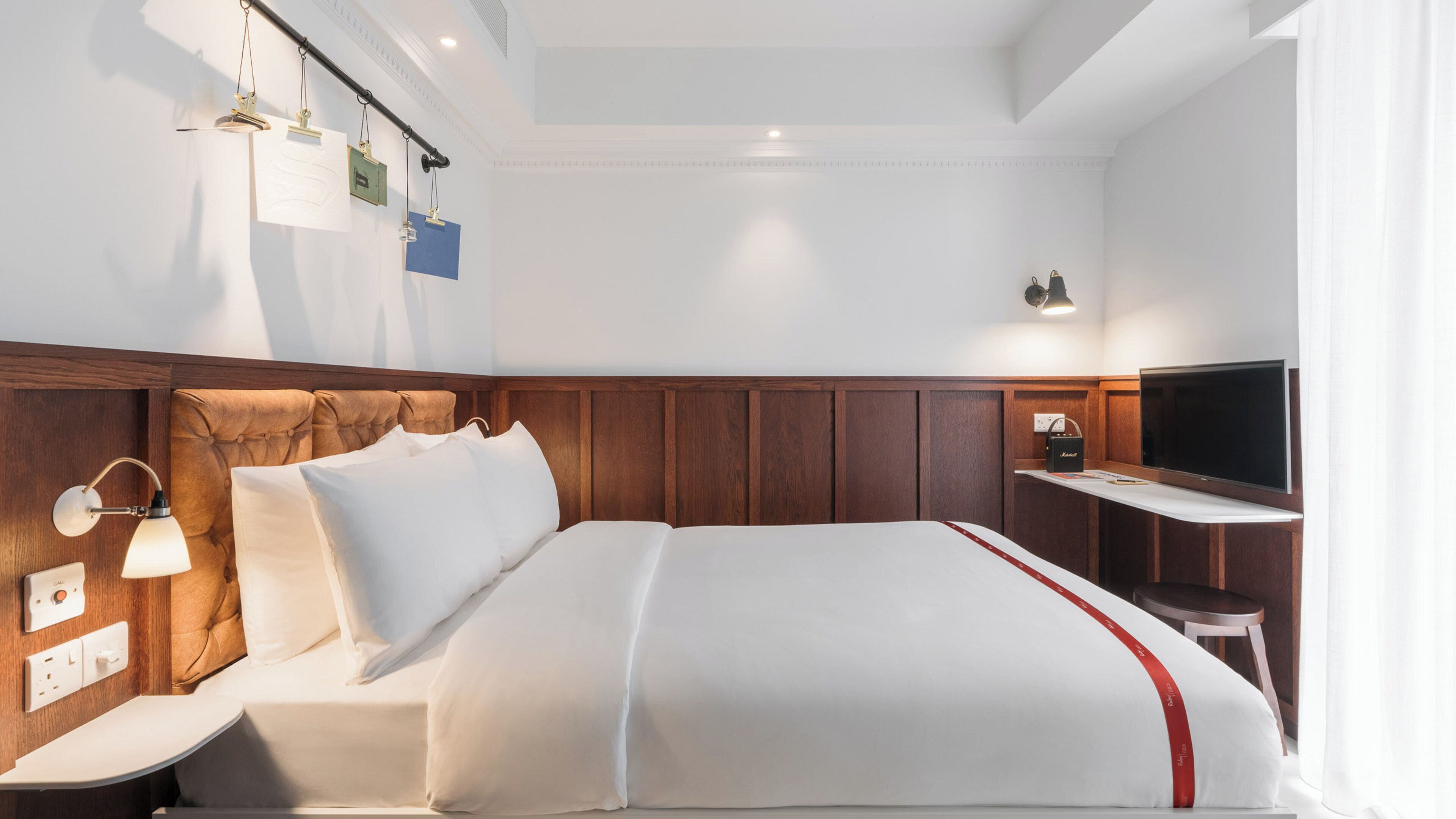Ein Hotelzimmer mit Bett, Nachttischlampen, Fernseher und einer Wandablage.