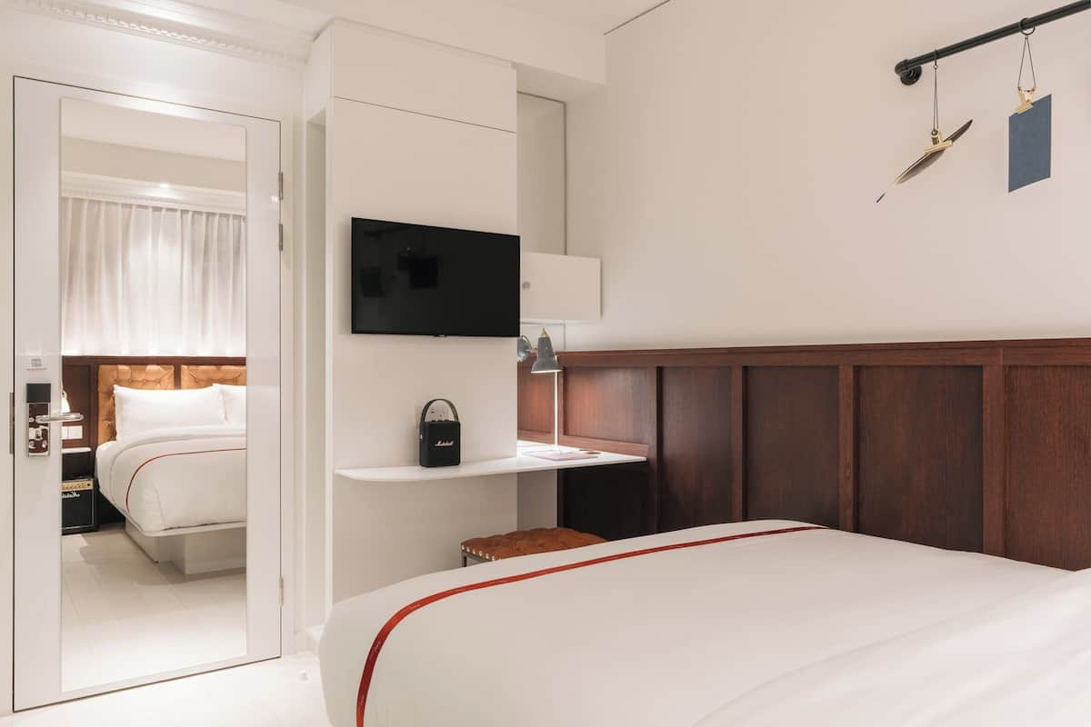 A hotel room with a bed, a TV mounted on the wall, a bedside table with a lamp, and a wooden headboard.