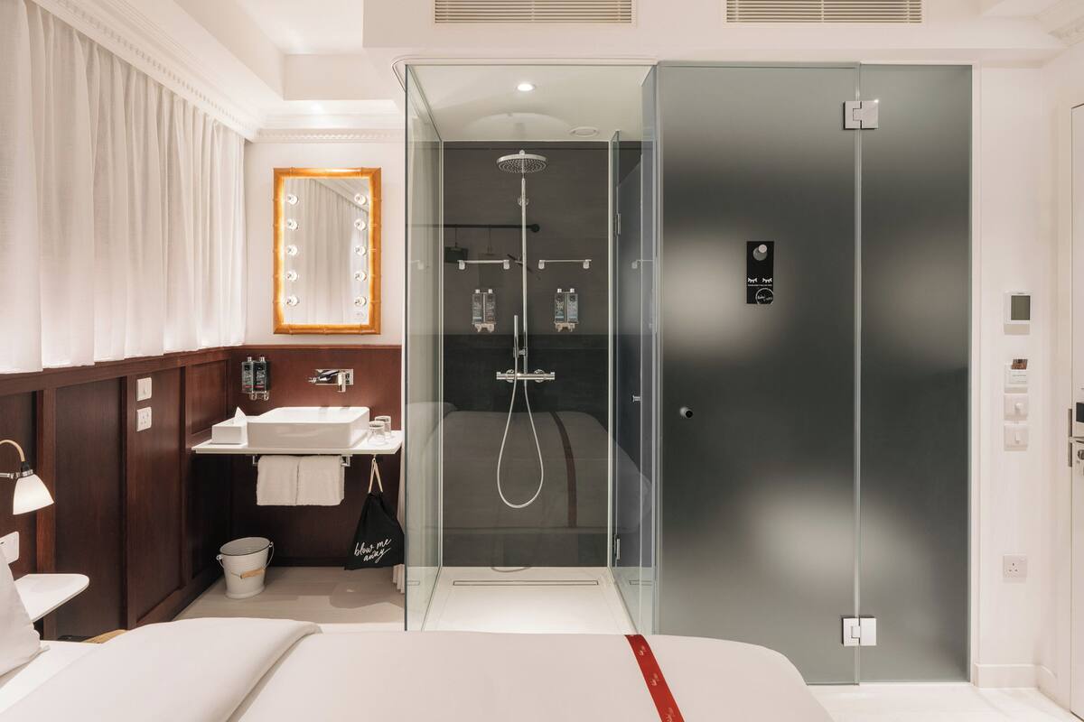 A modern hotel room with a large bed, a bathroom with a glass-enclosed shower, and a vanity with a mirror.